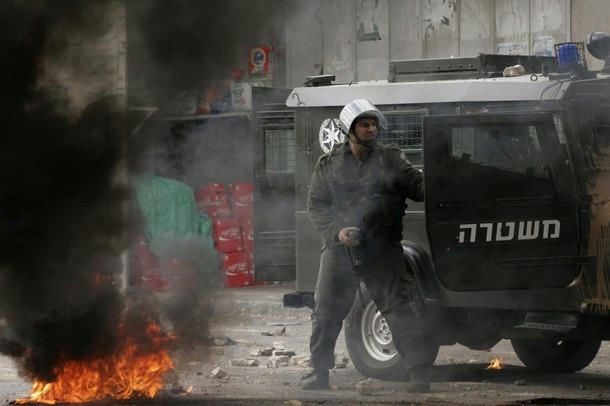 An Israeli border policeman takes cover behind a jeep door during violent 